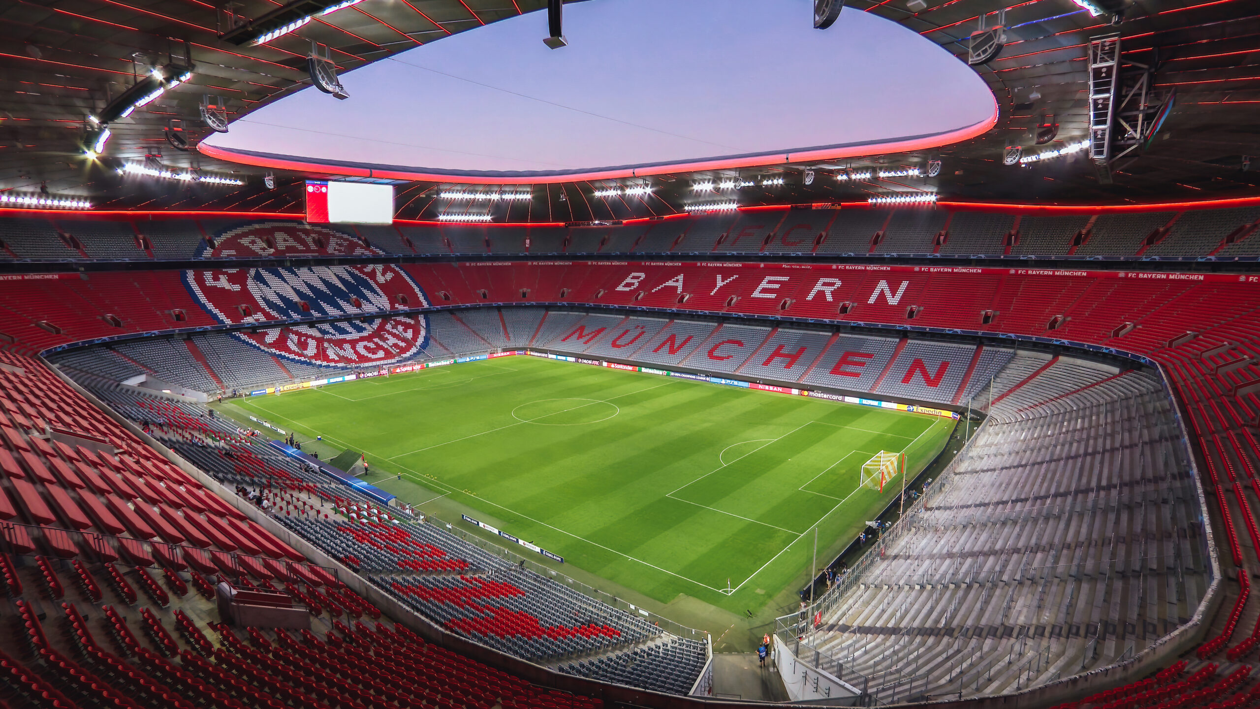 Inside Allianz Arena, home of Bayern Munich, illuminated in red, set to host the Champions League Final, featuring its modern architecture and world-class pitch