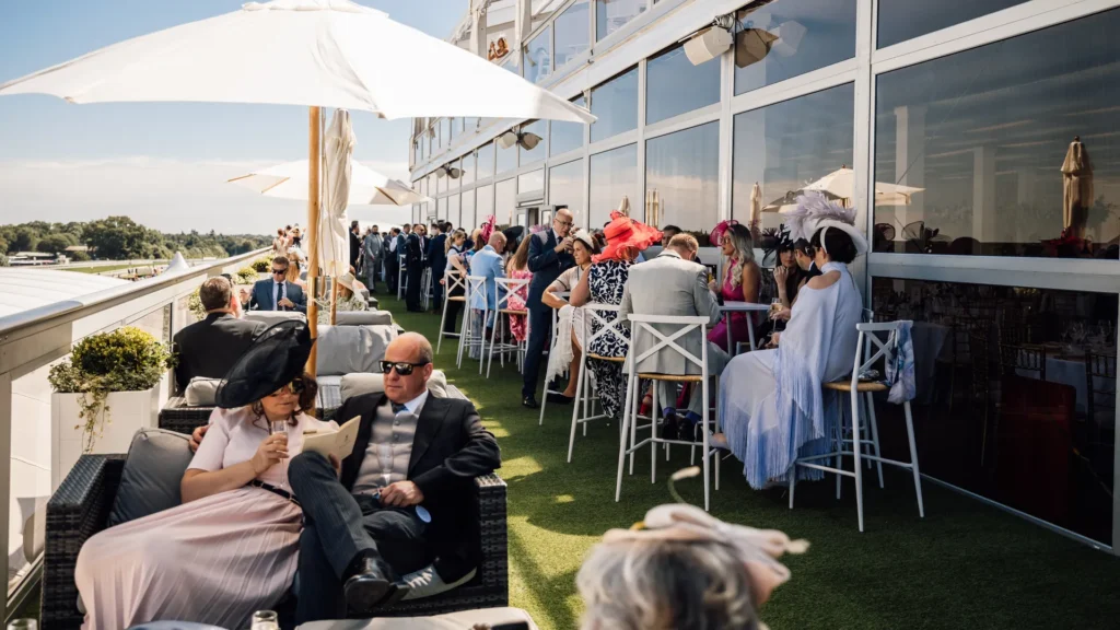 Elegant guests enjoying an outdoor hospitality experience at The Lawn Club, Royal Ascot, with stunning racecourse views, luxury seating, and stylish attire