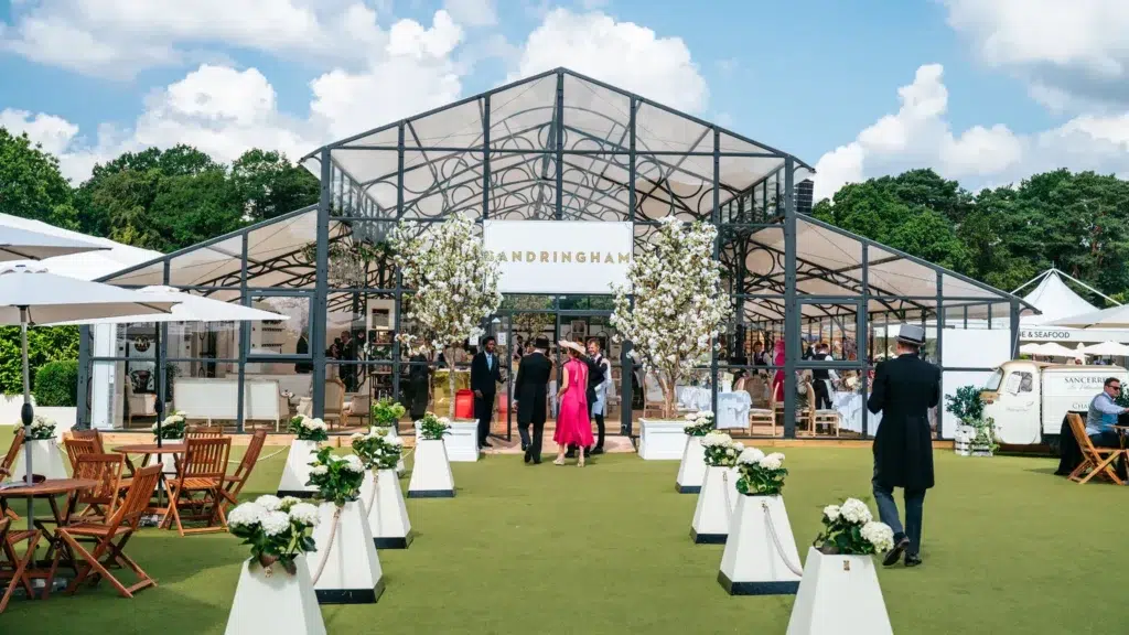 Royal Ascot Sandringham Restaurant – A stylish glass-fronted hospitality venue with elegant decor, lush floral arrangements, and well-dressed guests arriving for a luxury dining experience