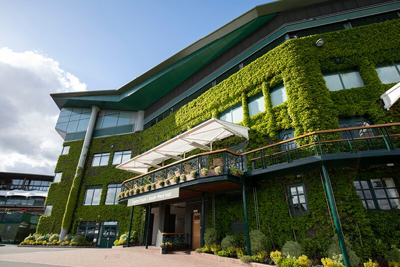Exterior view of Wimbledon Centre Court, featuring its iconic ivy-covered walls, elegant balconies, and modern architecture under a blue sky