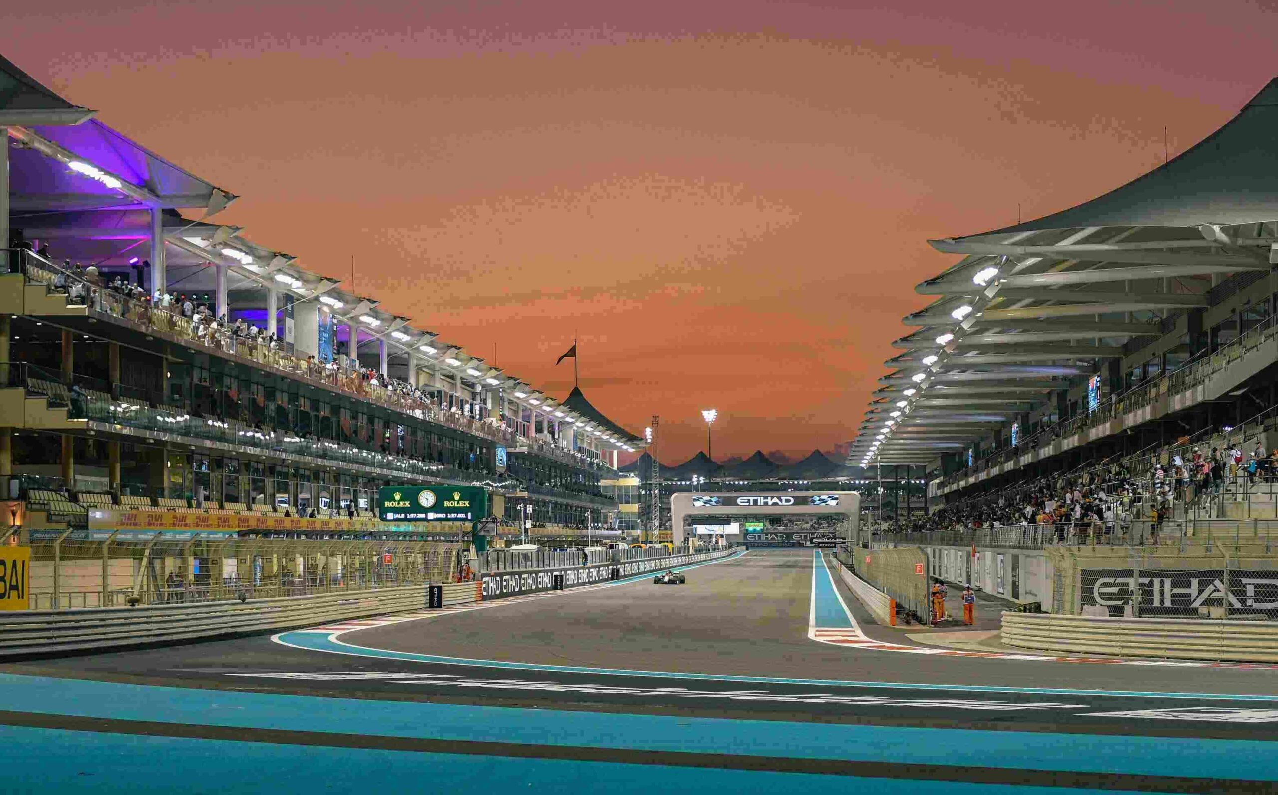 Yas Marina Circuit at sunset during the Abu Dhabi Grand Prix, showcasing illuminated grandstands and a dramatic evening sky