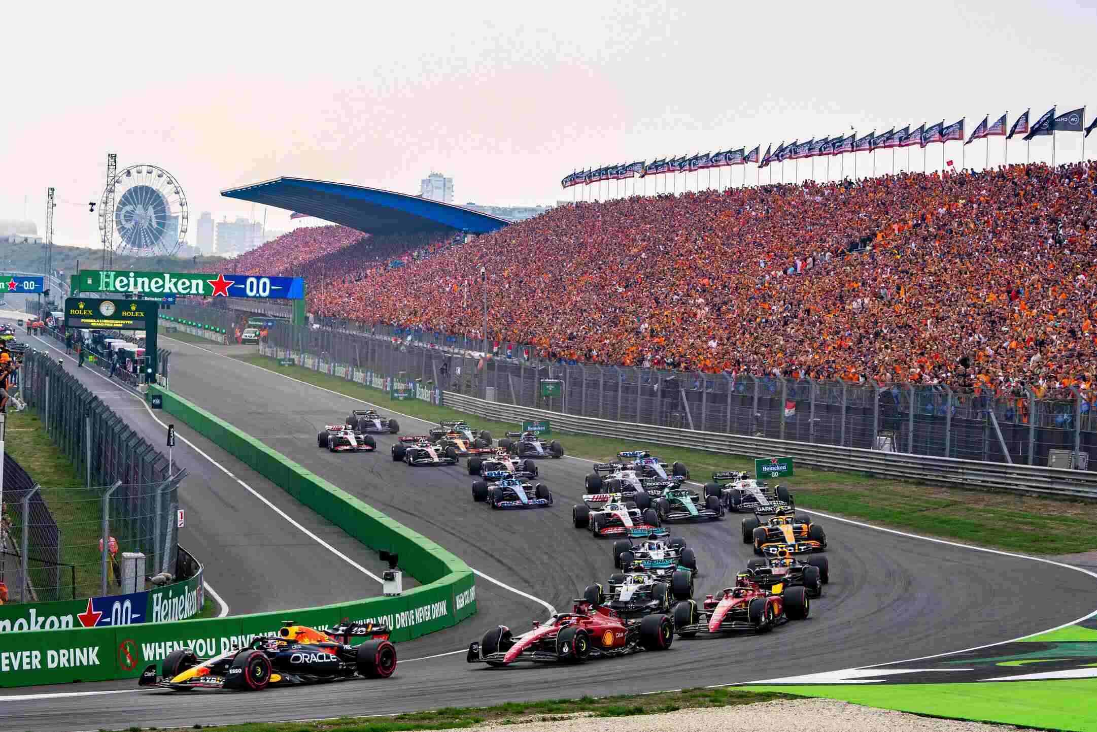 Formula 1 cars race through Zandvoort circuit at Dutch Grand Prix with packed orange-clad grandstands and a Ferris wheel in view