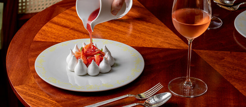 Elegant dessert at Wimbledon Courtside Restaurant, featuring a delicate pavlova with fresh fruit and berry sauce, paired with a glass of rosé