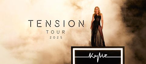 Promotional image for Kylie Minogue’s Tension Tour 2025. Kylie stands confidently in a sheer black gown on a lit platform with her signature displayed below, set against a dramatic, smoky backdrop