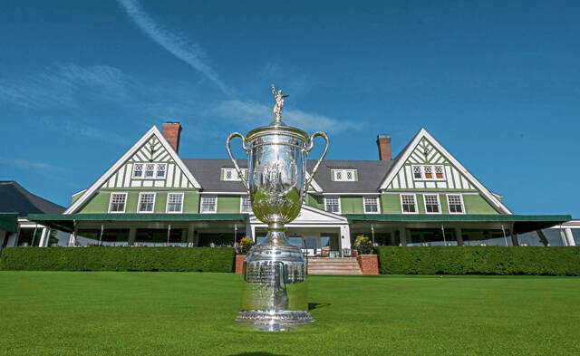 The U.S. Open Championship trophy displayed on a manicured lawn in front of a traditional country club building under a clear blue sky