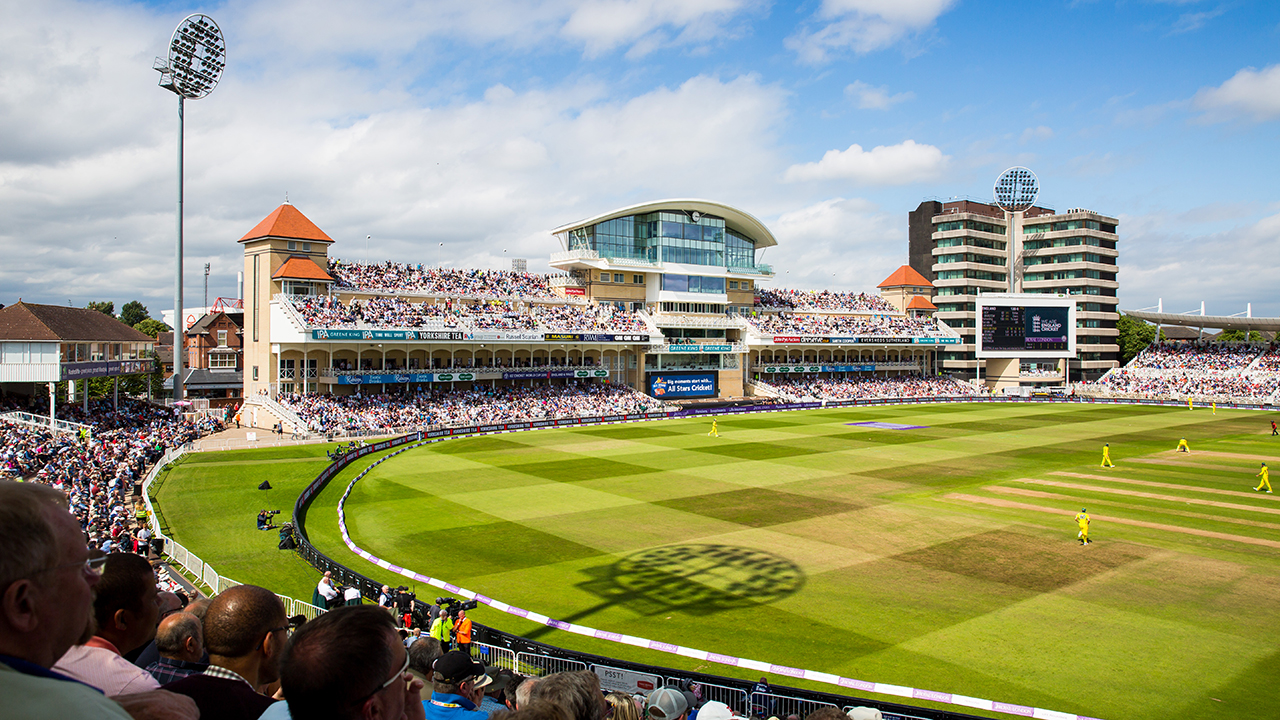 A packed Trent Bridge cricket stadium on a sunny day, with fans filling the stands and players in yellow kits on the field during a live match