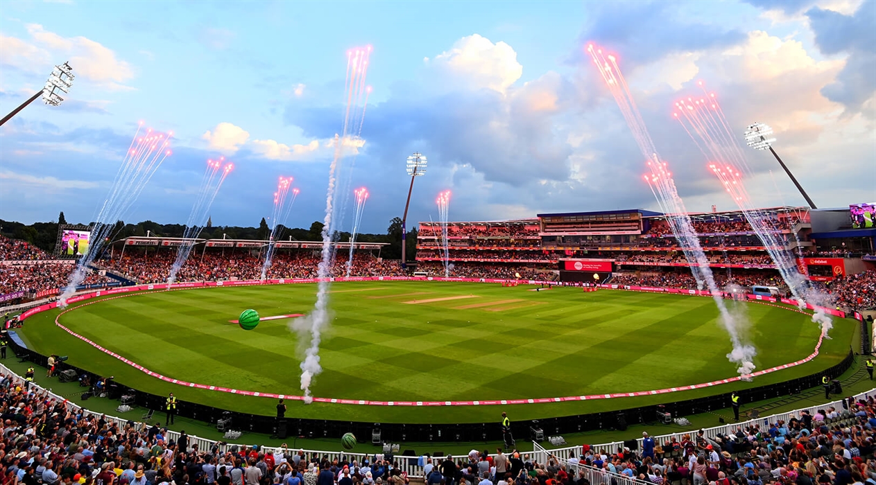 Edgbaston Stadium packed with spectators during a cricket match, with fireworks shooting into the sky and stadium floodlights illuminating the field at dusk