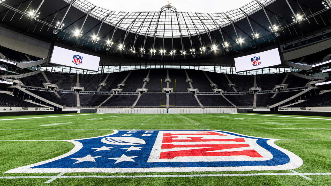 Empty NFL field setup at Tottenham Hotspur Stadium, showcasing the NFL logo at midfield and large display screens.