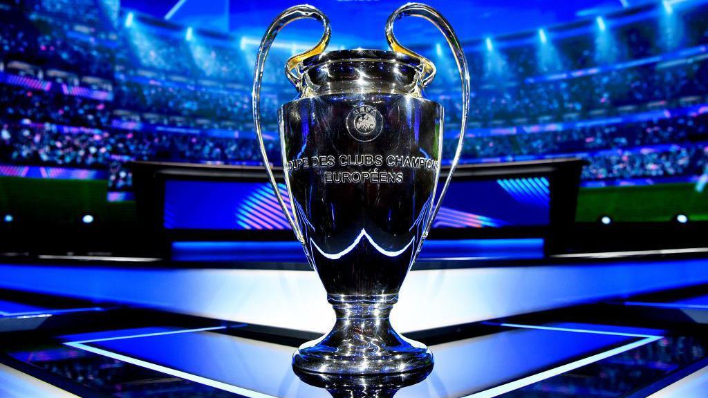 The UEFA Champions League trophy displayed in a stadium setting, illuminated by blue lights, symbolising Europe's most prestigious football competition.