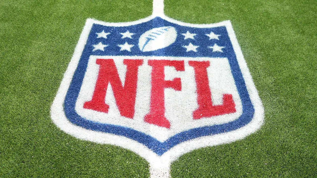 NFL logo painted on the turf of an American football field, featuring a football and stars above bold red lettering.