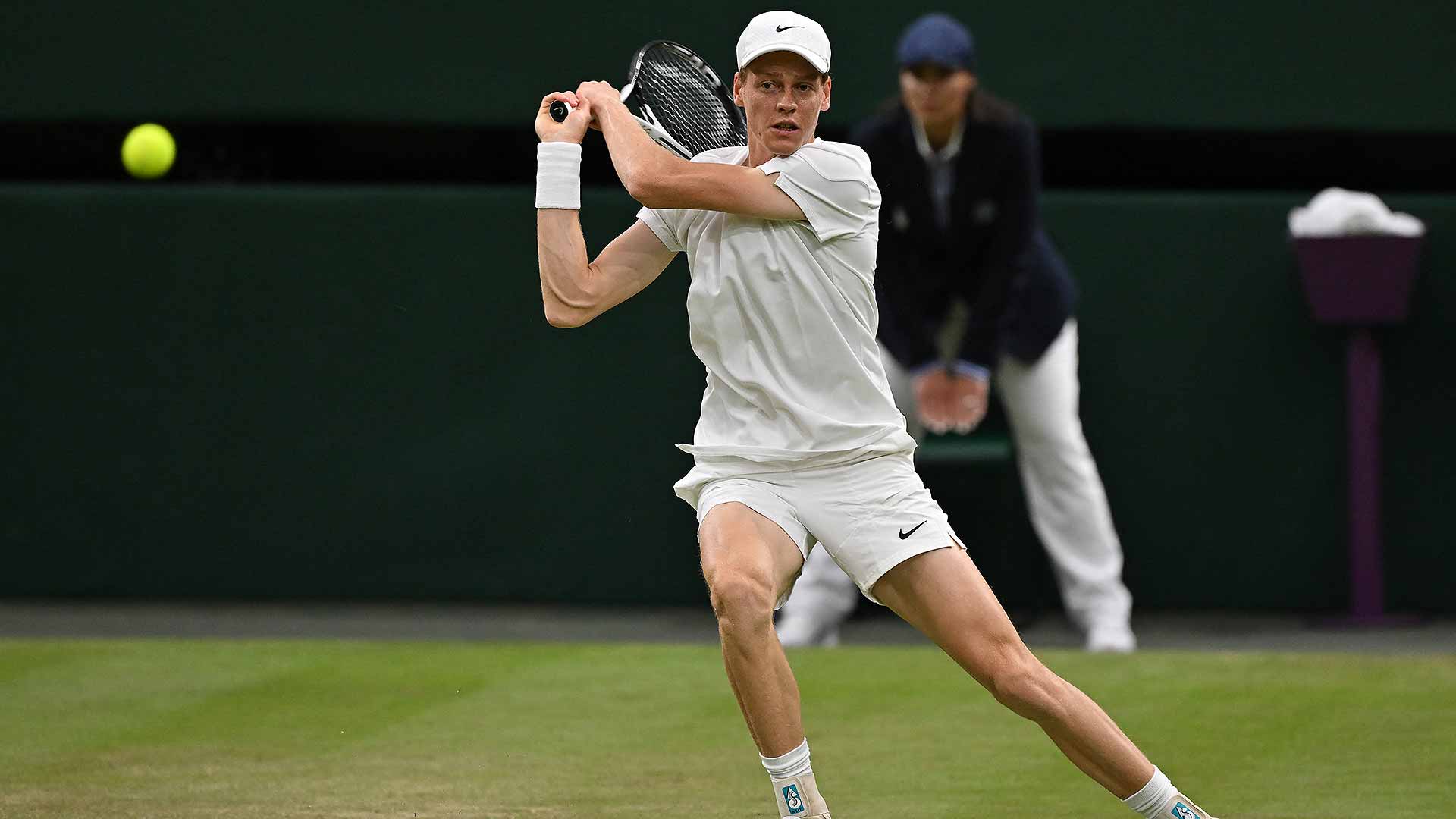 Jannik Sinner prepares to hit a backhand shot during a Wimbledon match, wearing an all-white Nike outfit on a grass court