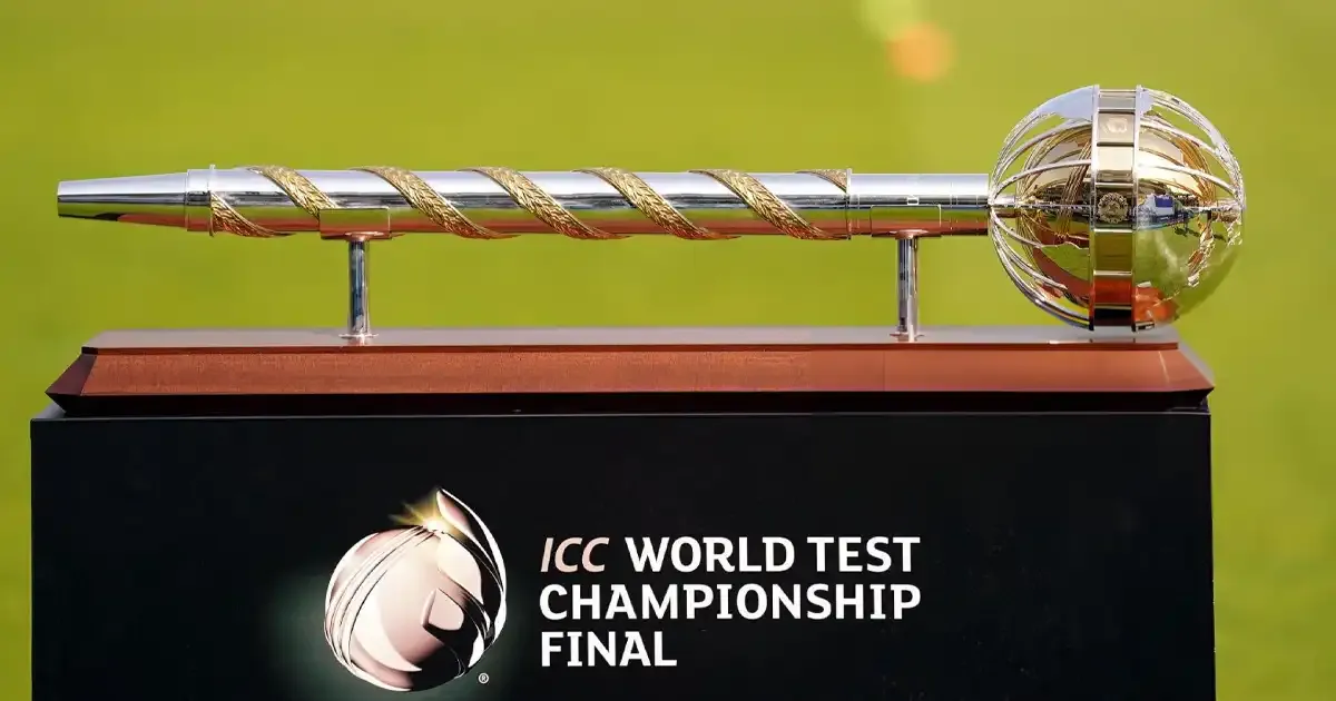 The ICC World Test Championship Final trophy displayed on a stand with the tournament’s logo, featuring a silver and gold mace against a blurred green field background